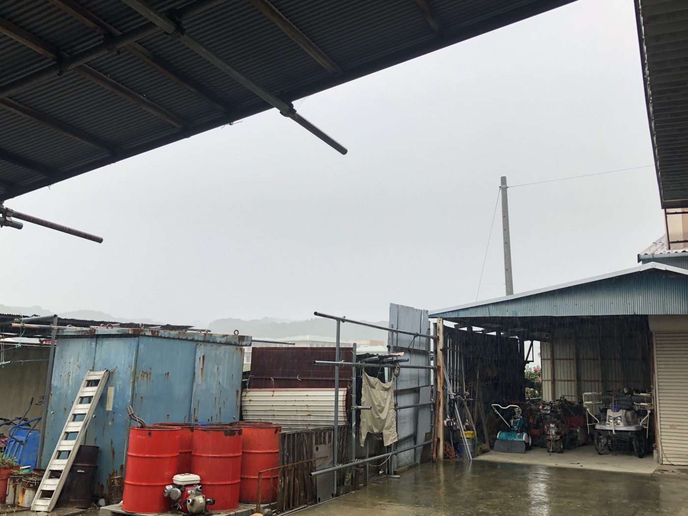 雨の日の大場農機の工場外観と農機具が並ぶ様子