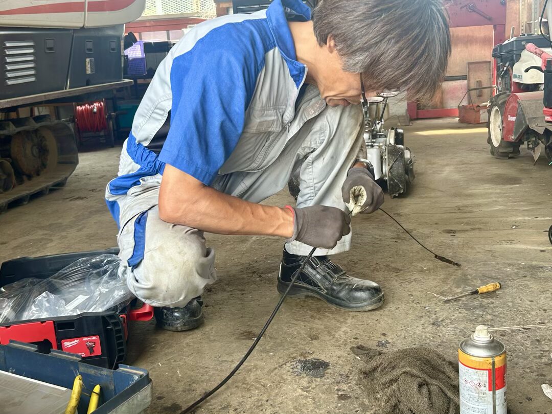 農機具の操作ワイヤーを布で拭き上げる整備士さん