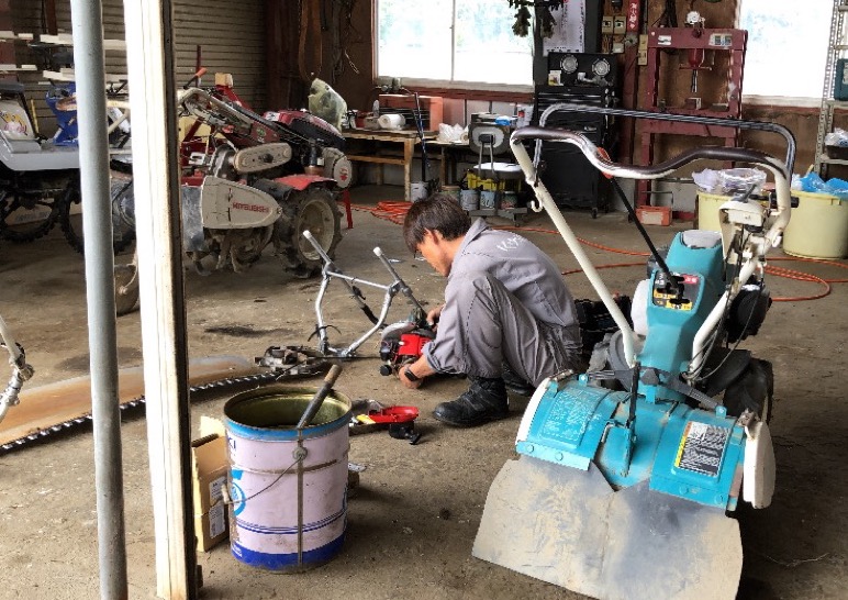 雨の日の農機具屋の作業場で、管理機の整備をする整備士