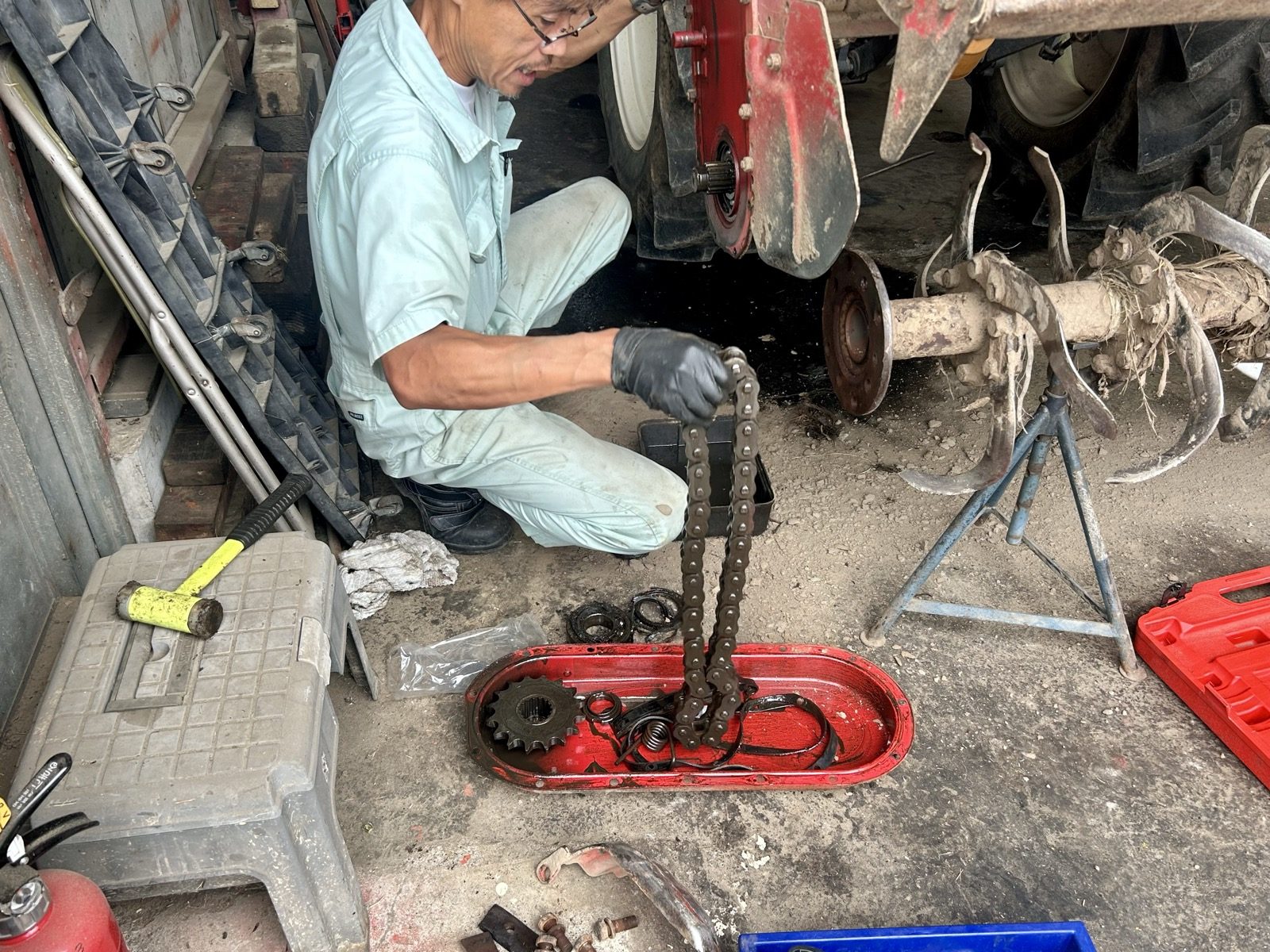 外したケースのふたの中にある歯車と、整備士さんが手で持ち上げているチェーン